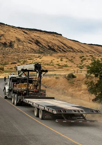 A photograph of a flatbed semi truck driving through a rural environment.