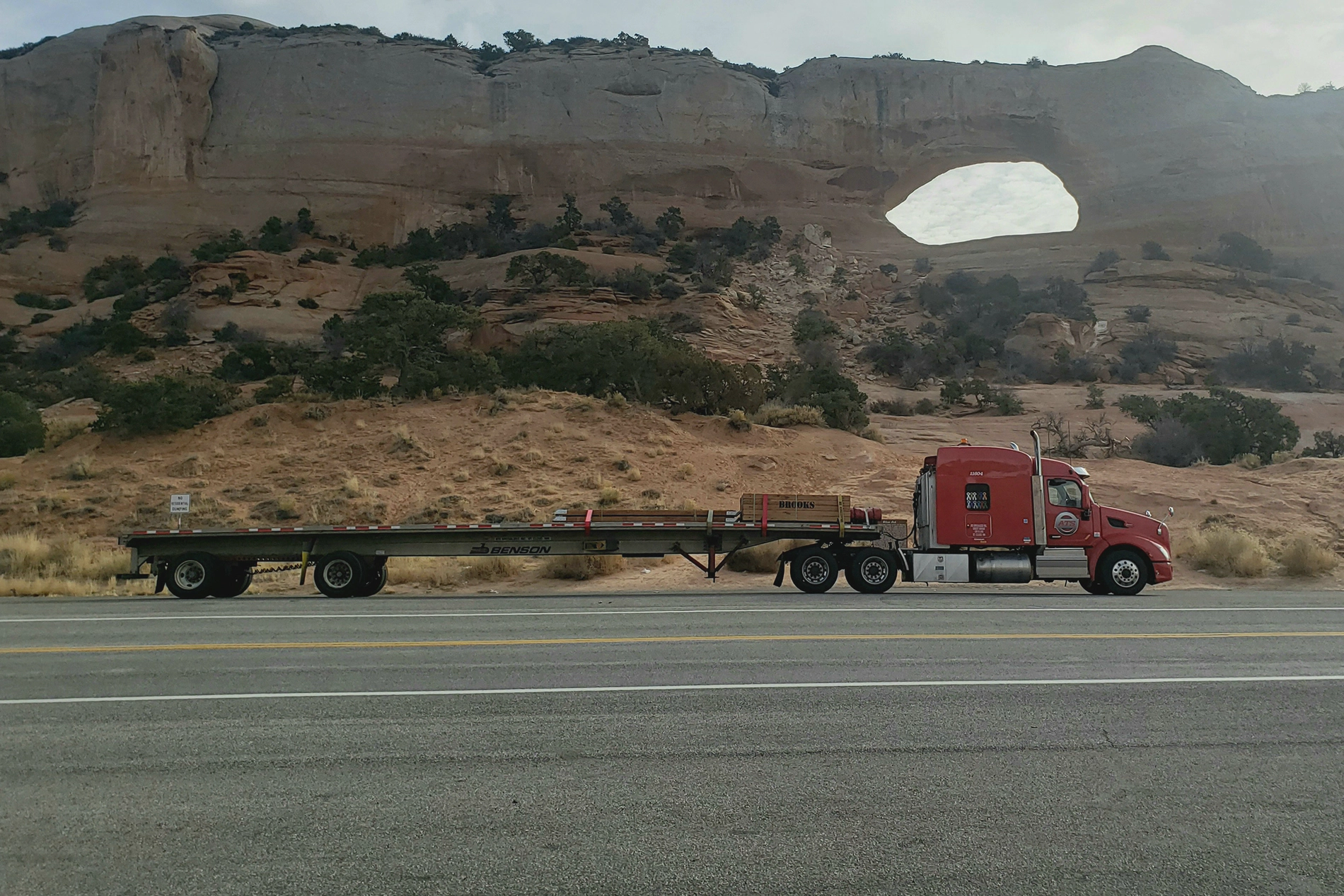A photograph of a flatbed semi truck driving in the desert.