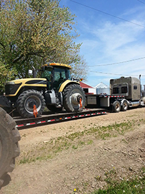 A photograph of a semi truck hauling a large farm tractor.